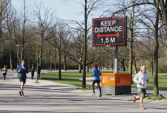 Люди в парке Вондела в Амстердаме бегут мимо знака, призывающего держать социальную дистанцию 1,5 м.  Амстердам, 22 марта ©Paulo Amorim/NurPhoto via Getty Images