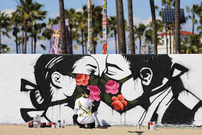 Художница Пони Вейв, напротив, напоминает жителям калифорнийской Венеции, что любовь любовью, а маски все же снимать не стоит, так как США  - лидер по количеству жертв пандемии. Фото: Getty Images/Mario Tama