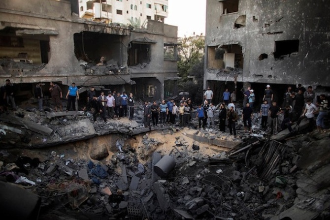 Палестинцы стоят вокруг кратера, образовавшегося в результате израильского авиаудара по дому в городе Газа.